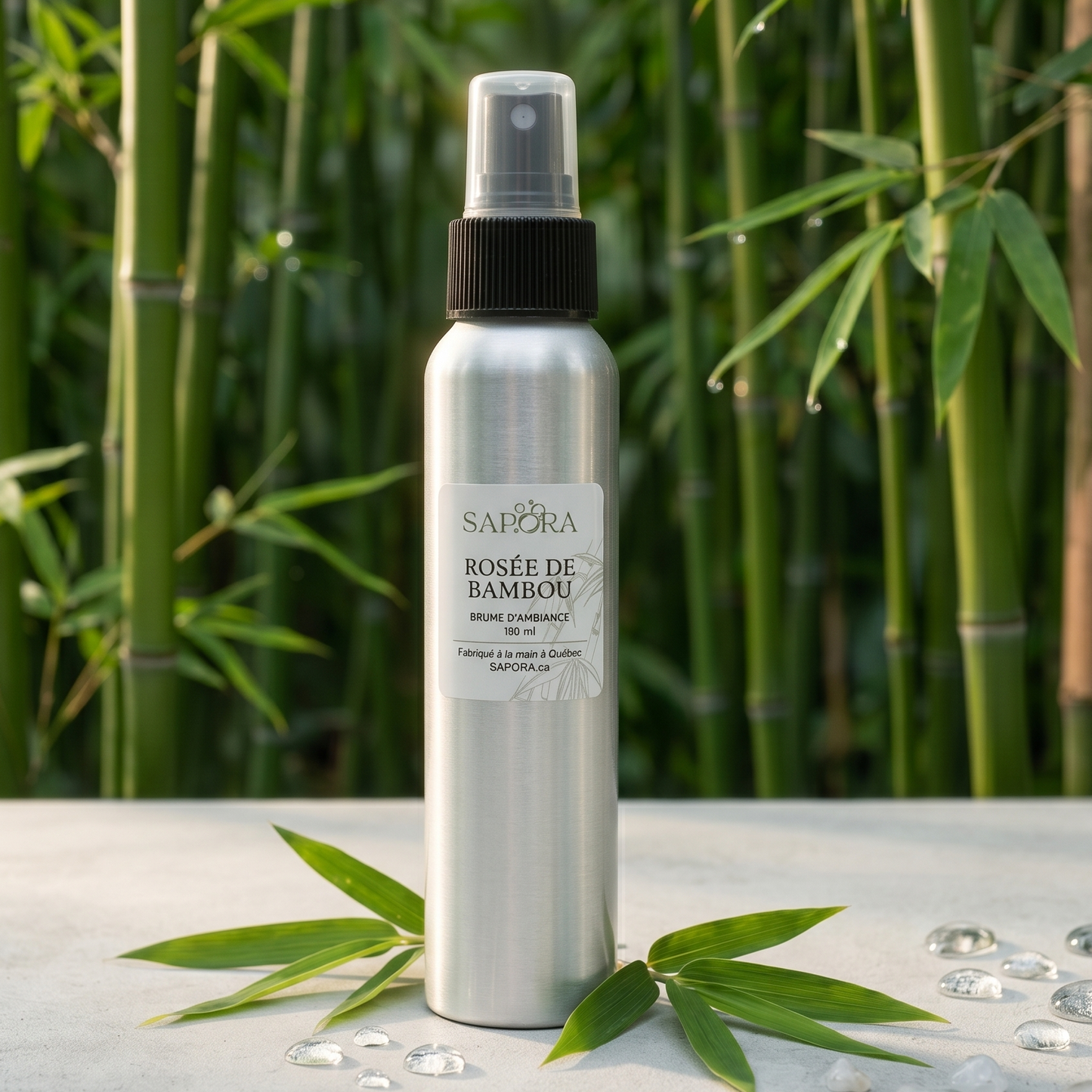 Bouteille de brume d'ambiance Rosée de Bambou de SAPORA en aluminium, présentée sur une surface blanche minimaliste avec des feuilles de bambou et des gouttes de rosée devant une forêt de bambous floue.