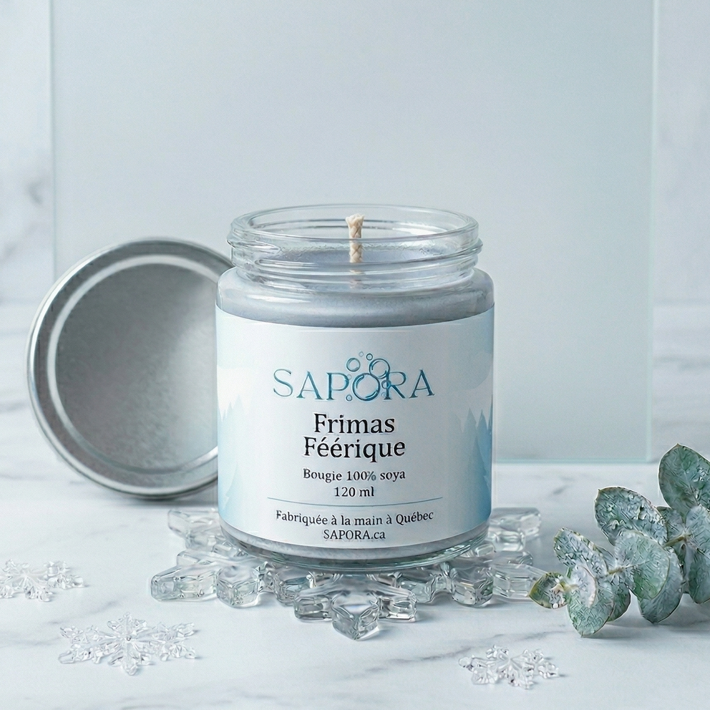 Bougie de soya Sapora Frimas Féérique dans un décor de Noël doux avec grenades fraîches, mûres et branches de conifères sur une table en bois d'acajou.