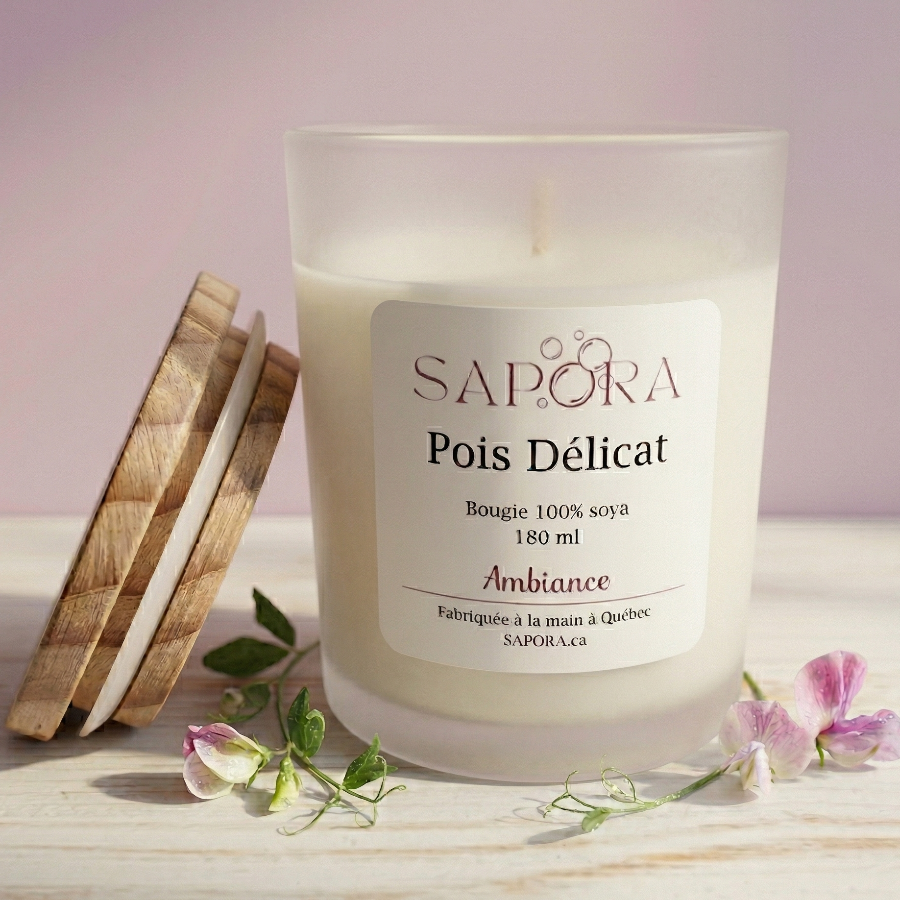 Bougie de soya Sapora Pois Délicat dans un pot en verre givré avec son couvercle en bois et des fleurs de pois de senteur sur une surface claire.