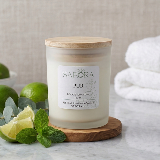 Bougie de soya Sapora "Pur" à la lime, menthe et eucalyptus, présentée sur un socle en bois dans un décor de spa chic avec des citrons verts frais, des feuilles de menthe, de l'eucalyptus et des serviettes blanches moelleuses.
