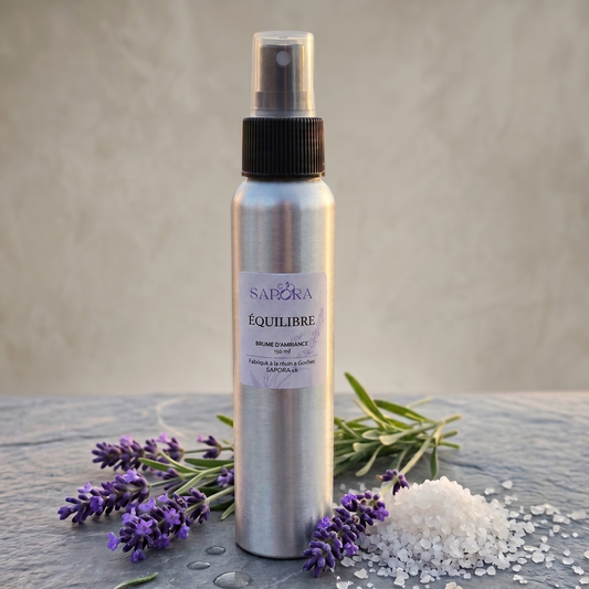 Bouteille de brume d'ambiance Équilibre de SAPORA en aluminium, posée sur une pierre naturelle avec des brins de lavande fraîche et un tas de sel de mer pur sur un fond neutre épuré.