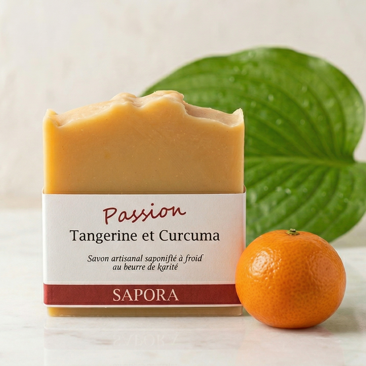 Savon artisanal au beurre de karité Sapora Tangerine et Curcuma posé sur un plateau en marbre blanc, accompagné d'une tangerine fraîche et d'une feuille verte sur un fond lumineux et épuré.