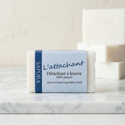 Savon détachant à lessive L'attachant de Sapora, savon artisanal blanc saponifié à froid présenté sur un socle en marbre blanc dans un décor minimaliste et épuré.