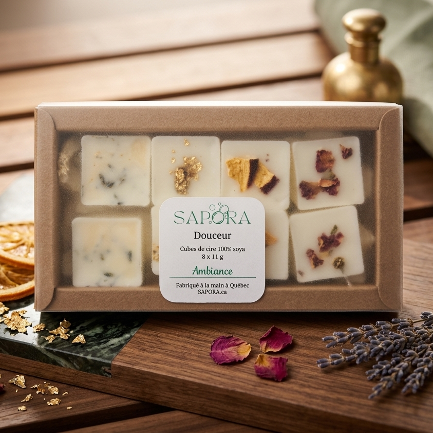 Coffret de fondants de cire de soya "Douceur" de Sapora dans sa boîte avec couvercle translucide, présenté dans un décor chic sur bois et marbre avec des tranches d'oranges séchées, de la lavande et des fleurs de sel dorées.