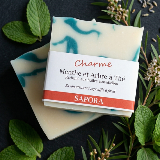 Savon naturel saponifié à froid aux huiles essentielles de menthe et arbre à thé. Décor chic et minimaliste avec feuilles de menthe verte, idéal pour une routine de soin de la peau naturelle.