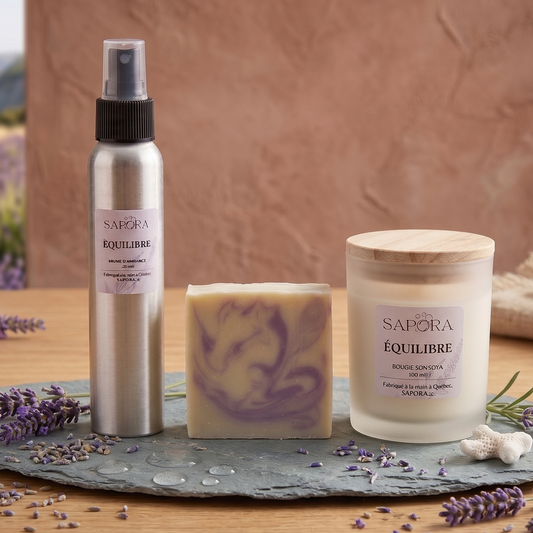 Ensemble cadeau Trio Équilibre de SAPORA comprenant une brume d'ambiance en aluminium, un savon artisanal marbré et une bougie de soya givrée, présentés sur une ardoise naturelle avec des fleurs de lavande séchées et une vue sur un champ de lavande au bord de la mer.